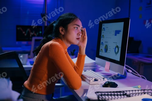 Preview: Stressed Asian businesswoman looking at financial charts on computer in office at night