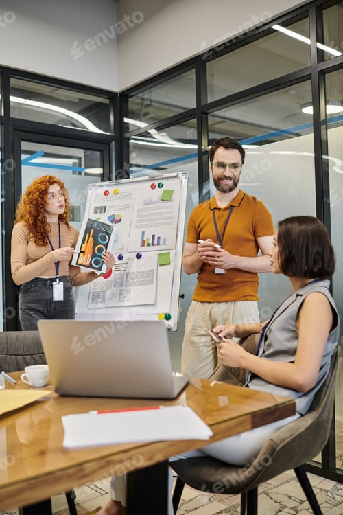 Preview: redhead manager with infographics near bearded colleague and businesswoman in meeting room