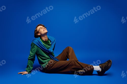 Preview: Young man in stylish attire enjoying the moment against a vibrant blue backdrop