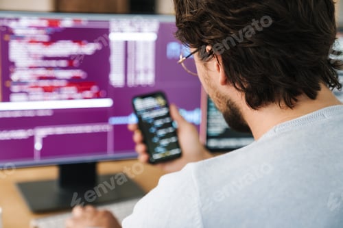 Preview: Image of programmer man using smartphone while working with computers