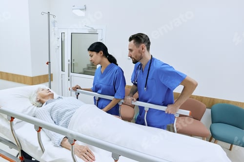 Preview: Two nurse supporting elderly woman lying on medical gurney in hospital hall with IV drip. Patient
