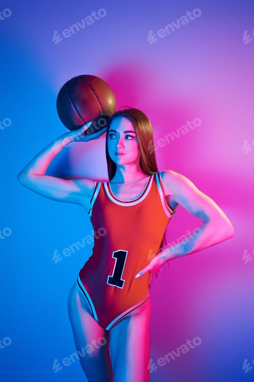 Preview: Holds ball. Fashionable young woman standing in the studio with neon light