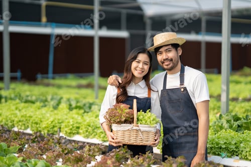 Preview: Happy ypung Asian couple smailing at hte camera while standing in a hydroponics farm.