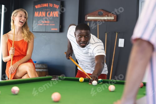 Preview: A young African American man focuses on a pool shot as a young Caucasian woman watches, laughing