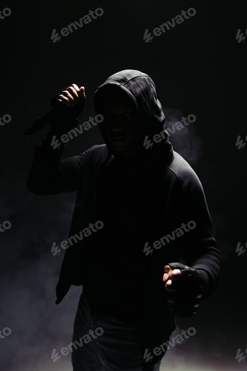 Preview: Silhouette of african american man in hood and gloves holding knife on black background with smoke