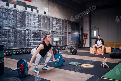Preview: Young man watching woman lift barbell in gym