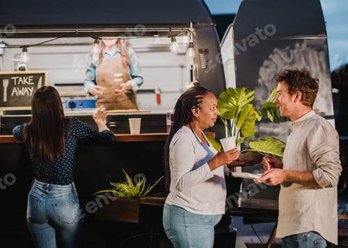 Preview: Diverse friends with food and drink speaking in park in evening