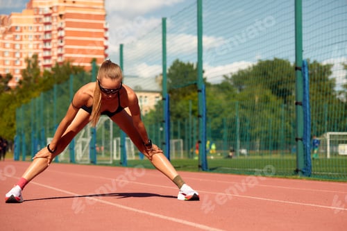 Preview: Young woman runner warming up at the racetrack. Fit runner workout, stretch her muscle and warming