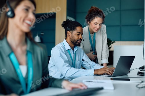 Preview: Female executive manager supervising black colleague who is working on laptop in the office.