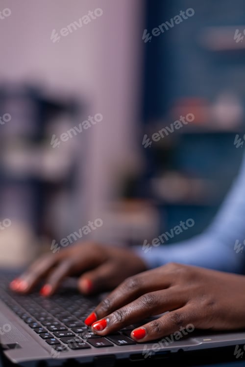 Preview: African american in living room using laptop computer sitting at desk at night .