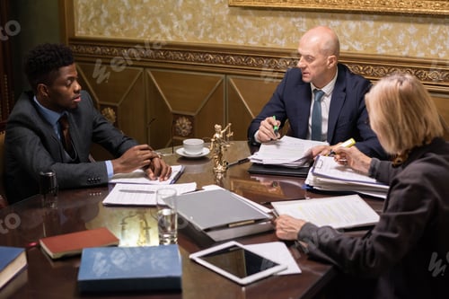 Preview: Group of intercultural lawyers having discussion by table in boardroom
