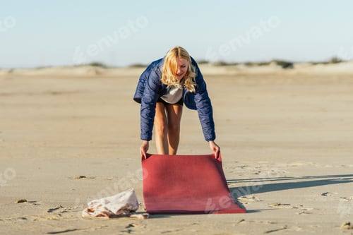 Preview: Female rolling out a yoga mat on the beach