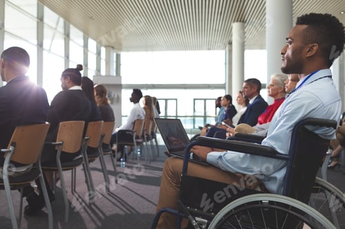 Preview: Side view of young disabled mixed race businessman using laptop during seminar in office building