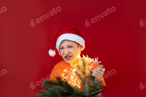 Preview: a boy in Christmas clothes is holding a Christmas tree, he grimaces and shows his teeth