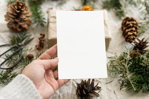 Preview: Christmas card mock up. Hand holding empty greeting card on rustic table with fir branches