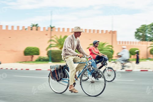 Preview: Man leisurely cycling past an orange wall under a cloudy sky