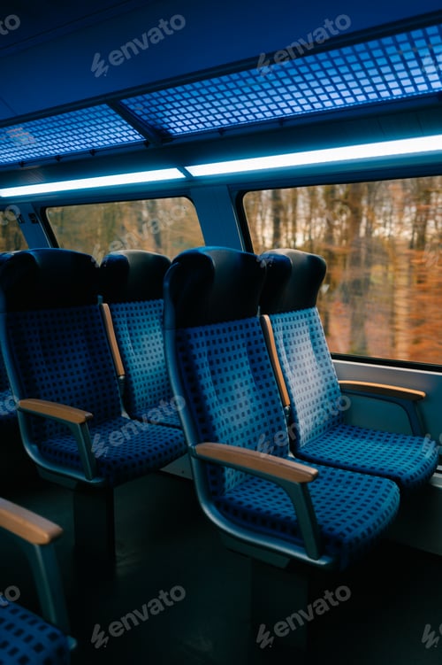 Vista previa: Empty modern train seats with a blue interior, illuminated by soft overhead lighting