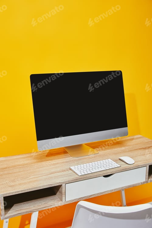 Preview: Computer at wooden table with chair near bright yellow wall