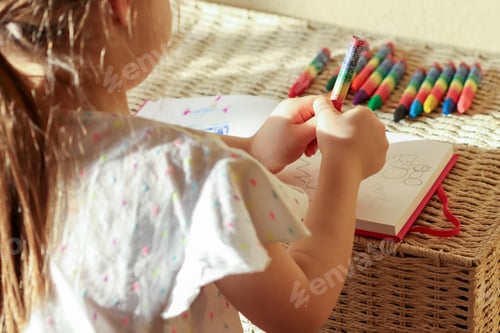 Preview: Little girl 6 years old draws with wax crayons in a sketch book