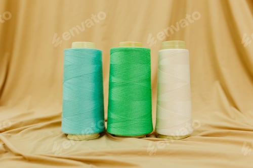 Preview: four spools of various colored thread for sewing, on a plain cloth backdrop