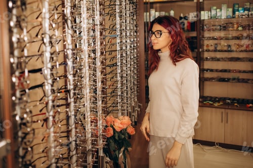 Preview: eyesight and vision concept - young business woman choosing glasses at optics store
