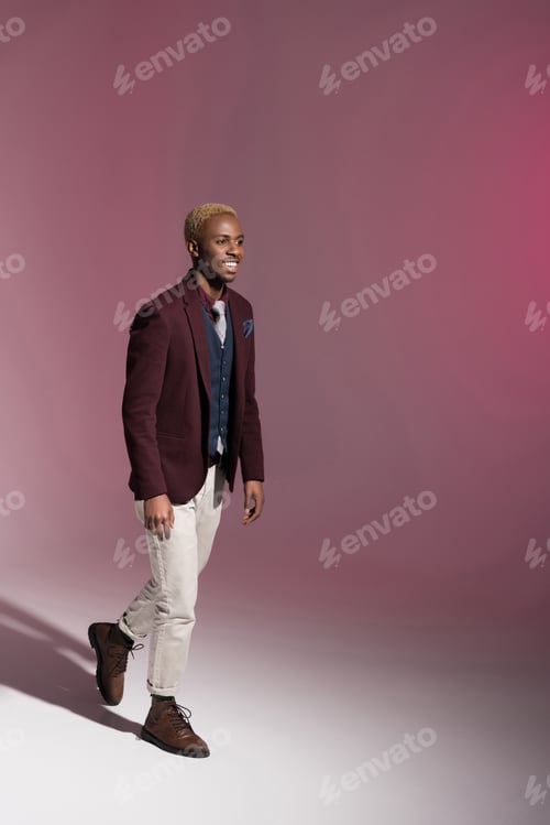 Preview: Smiling african man in red jacket walking on pink background