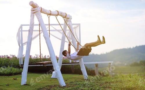 Preview: Teenage boy sit on white swing and swing happily in the nature closeup blur mountainside background