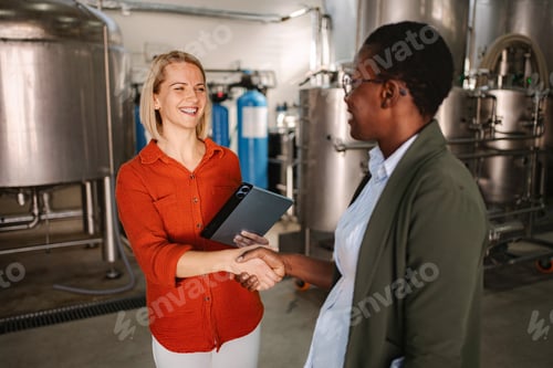 Preview: Businesswomen shaking hands in industrial brewery facility