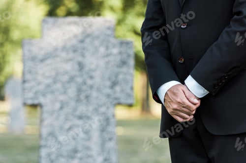 Preview: cropped view of elderly man standing near tombs with clenched hands