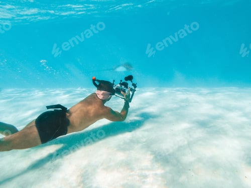 Preview: Man taking underwater footage of stingray with a professional camera equipment in underwater case