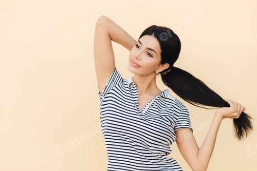 Preview: Pensive dark haired female makes pony tail, has full lips and pleasant appearance