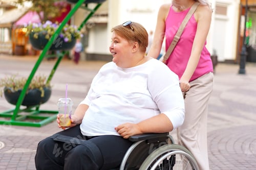 Preview: Young woman helping mature woman in wheelchair in the city