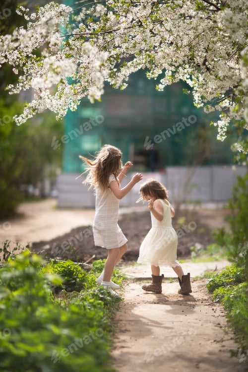 Preview: Tender young girls children jump and run near the blossoming cherry. Expression happy childhood