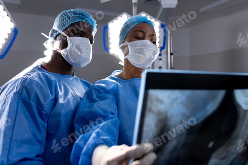 Preview: African american male and female doctors with face masks looking at x-rays in hospital