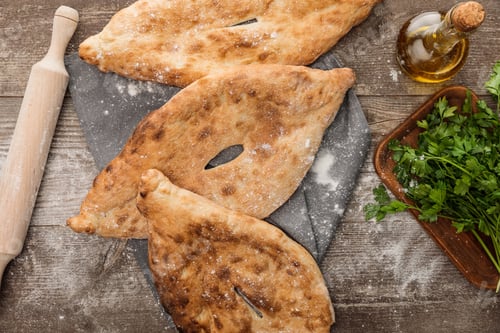 Preview: top view of lavash bread on gray towel near rolling pin, fresh parsley and olive oil on wooden table