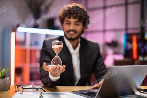 Preview: Confident businessman in formal suit sitting at desk with modern laptop and holding hourglass