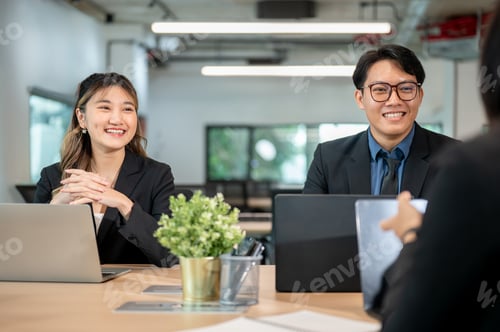 Preview: Businessman and woman sitting with laptop and talking with coworker at wooden table in meeting room.
