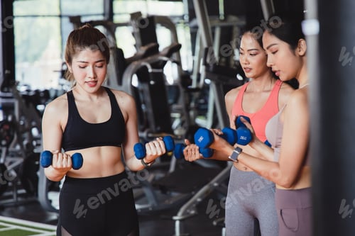 Preview: Group of Asian Young woman talking and smiling while lift dumbbells at fitness gym