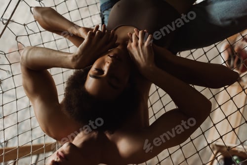 Preview: top view of passionate interracial couple holding hands while lying in hammock in workshop