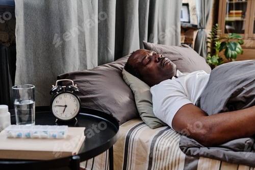 Preview: Aged African American man in white t-shirt sleeping under gray cover on bed