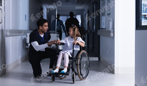 Preview: Diverse male doctor talking with girl in wheelchair in hospital corridor