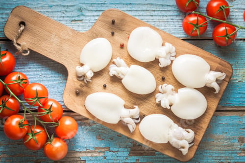Preview: Raw babies cuttlefish on a cutting board with tomatoes