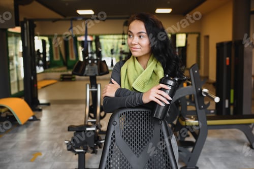 Preview: Young woman drinking water and taking a break after workout in gym,