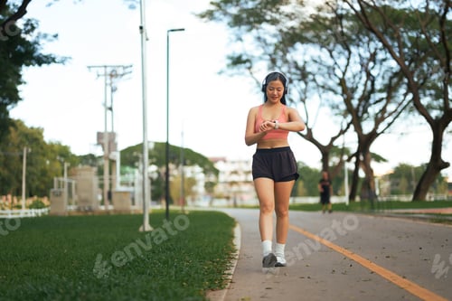 Preview: Woman jogging in park checking fitness tracker