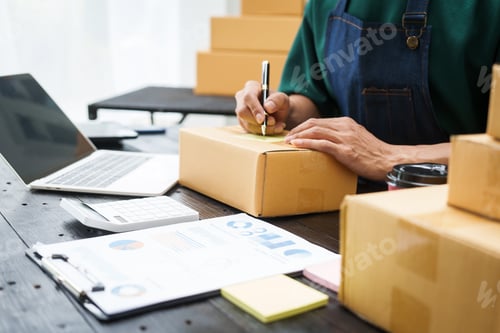 Preview: A man is working at his desk, preparing parcel boxes for shipment. He checks packs items carefully