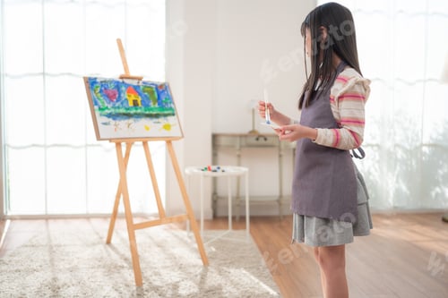 Preview: A little girl painting on an easel with focus and creativity in a living room at home