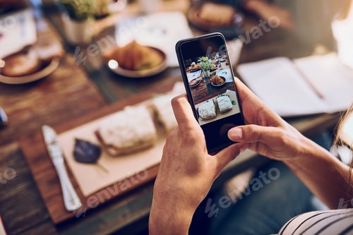 Preview: Cropped shot of a woman taking a picture on her phone of her food