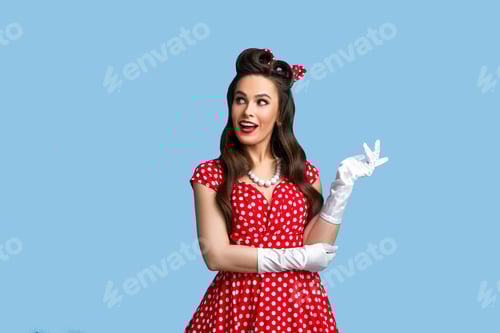 Preview: Seductive young woman in pinup retro style outfit looking aside and smiling on blue studio