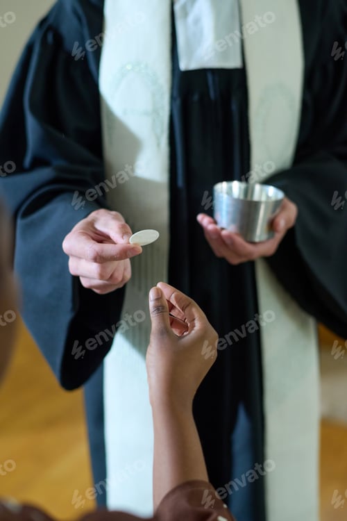 Preview: Hand of young Catholic priest in cassock passing unleavened bread to woman