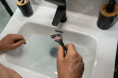 Preview: Unrecognizable man's hands hold razor over clogged sink filled with water